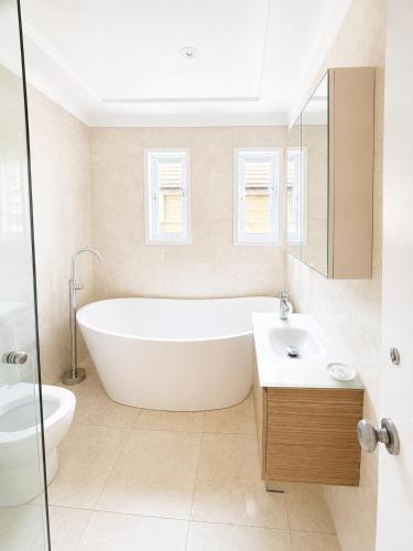 a white bathroom with a tub and a sink at Unique beach flat with own carpark area in Freshwater