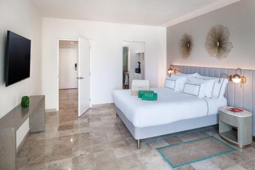 a white bedroom with a large bed and a tv at Meliá Casa Maya Cancún in Cancún