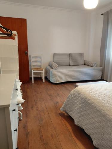 a bedroom with a bed and a couch and a chair at De Cá - suite com acesso independente e kitchenette in Lousã