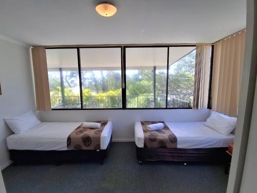 two beds in a room with two large windows at Tower Court Motel in Hervey Bay