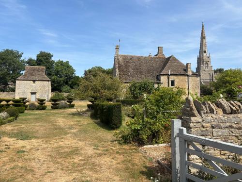 an old stone house with a fence and a church at Canutes Field bell tent in Nassington