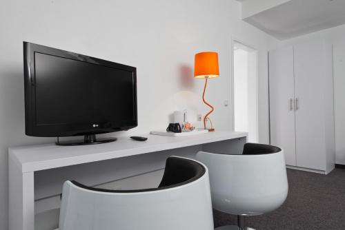 a living room with a tv and two white chairs at Wyndham Garden Düsseldorf City Centre Königsallee in Düsseldorf