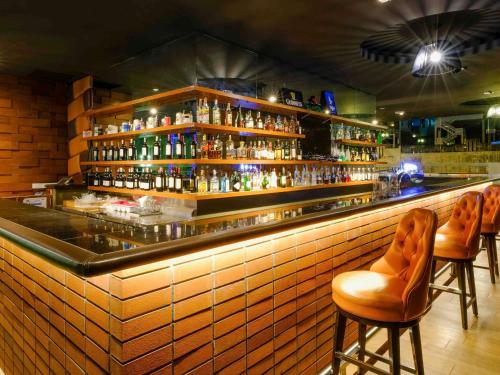 a bar with orange bar stools and bottles of alcohol at Mercure Penang Beach in George Town