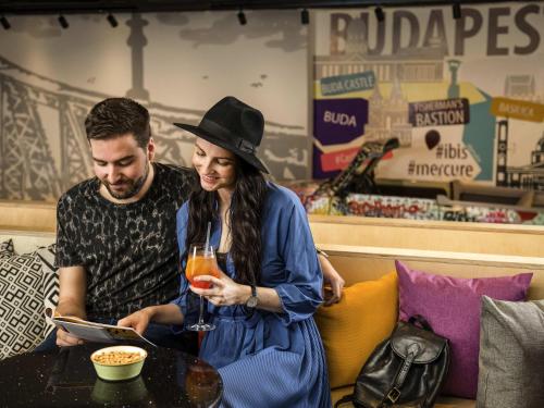 a man and a woman are looking at a book at ibis Budapest Castle Hill in Budapest