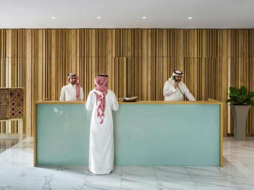 a woman standing in front of a counter with two men at Adagio Jeddah City Center in Jeddah