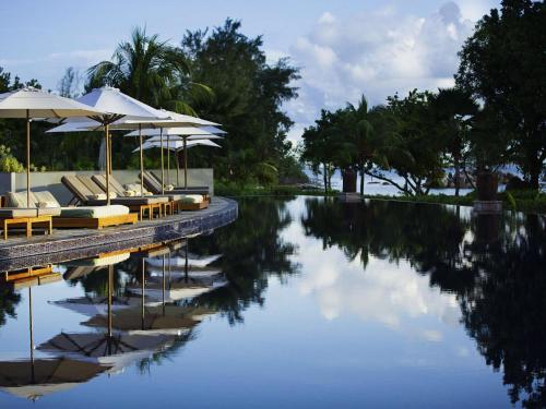 a pool with lounge chairs and umbrellas next to the water at Raffles Seychelles in Baie Sainte Anne