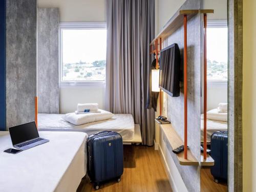 a hotel room with two beds with luggage and a laptop at ibis budget Leme SP in Leme
