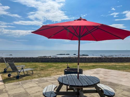a picnic table with a red umbrella and a chair at Driftwood in Mainsriddle