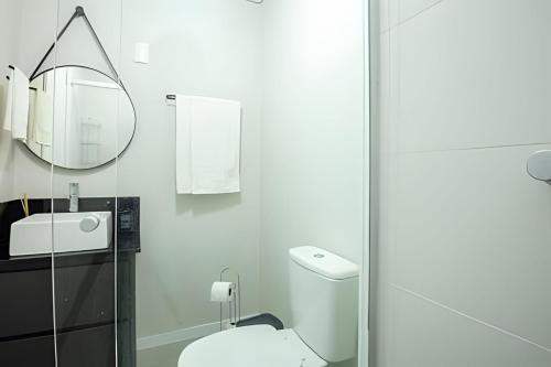 a white bathroom with a toilet and a mirror at Studio 907 Flow Live - Parque Una + garagem in Pelotas