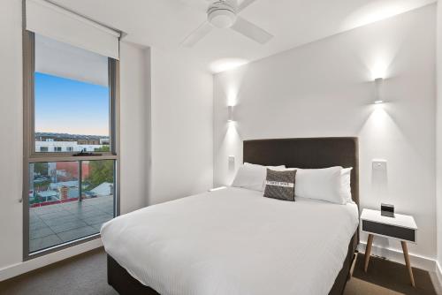 a bedroom with a white bed and a large window at District Apartments Fitzroy in Melbourne