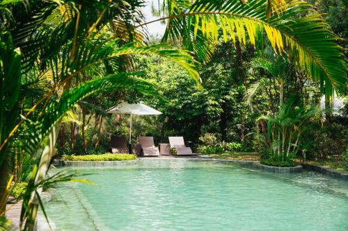 a swimming pool with two chairs and an umbrella at AMAYA HOME - Lodge, Spa & Restaurant Sóc Sơn in Sóc Sơn