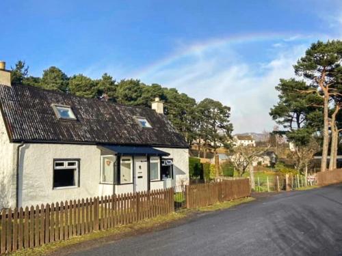 a white house with a fence on the side of a road at Broom Cottage in Newtonmore