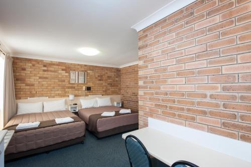 a bedroom with two beds and a brick wall at Buckaroo Motor Inn in Warwick
