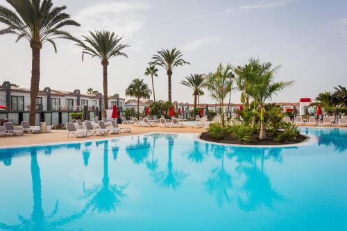 a large swimming pool with palm trees and lounge chairs at Sholeo Lodges Maspalomas in Playa del Ingles