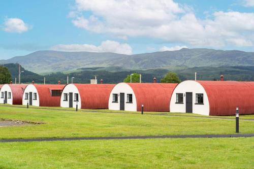a row of red and white buildings with mountains in the background at Cultybraggan Hut 35 in Comrie