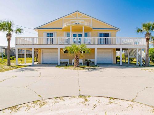 a yellow house with a balcony and palm trees at Sunglow Bungalow in Pensacola Beach