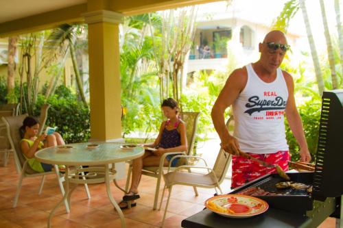 a man cooking food on a grill with people sitting at Monte Carlo Luxury Condominiums in Jacó