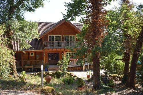 a large wooden house with a porch and trees at Trésor en Bois Chambres d'Hôtes in Autoire