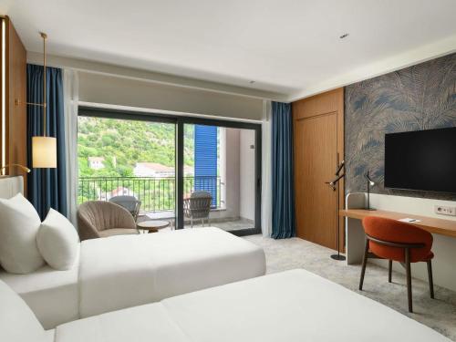 a hotel room with two beds and a desk and a television at Mövenpick Hotel & Residences Teuta Kotor Bay in Kotor