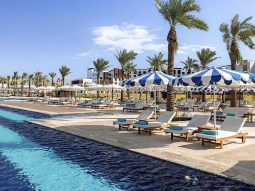 a pool with lounge chairs and umbrellas next to a resort at Rixos Murjana - Ultra All Inclusive in King Abdullah Economic City