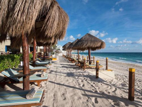 a row of straw umbrellas and chairs on a beach at Club Regina Cancun in Cancún