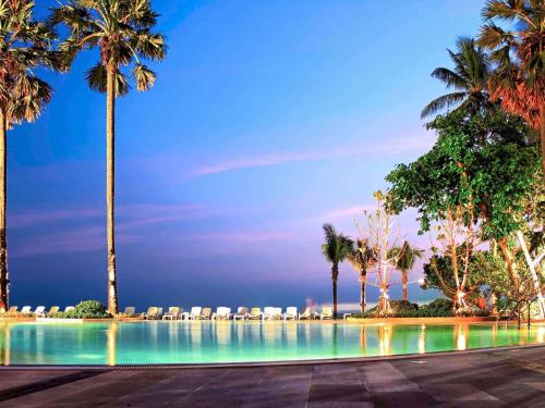 a swimming pool with palm trees and lounge chairs at Novotel Rayong Rim Pae Resort in Klaeng