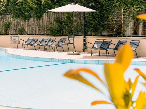 a row of chairs and an umbrella next to a swimming pool at Novotel Roma Est in Rome