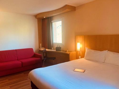 a hotel room with a bed and a red couch at ibis Loriol Le Pouzin in Le Pouzin