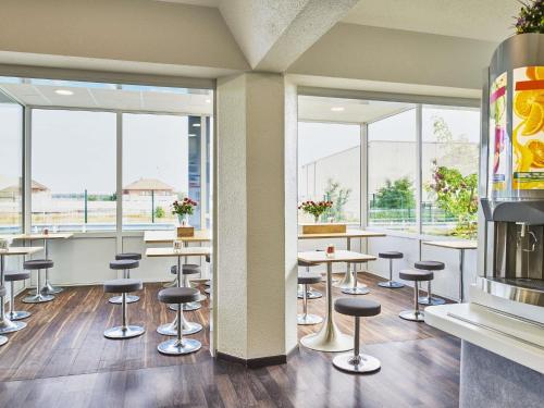 a restaurant with stools and tables and windows at ibis budget Santeny in Santeny