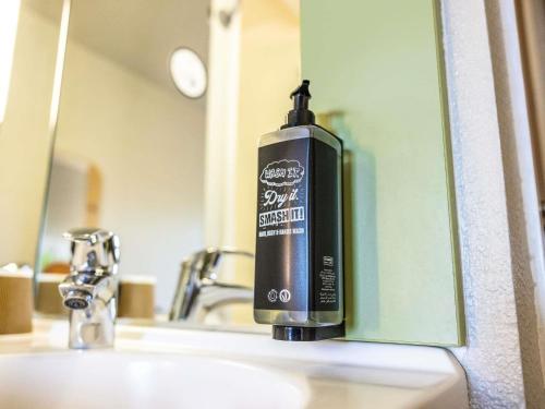 a soap dispenser on a bathroom sink in front of a mirror at ibis budget Bordeaux Sud in Villenave-dʼOrnon
