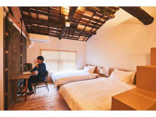 a person sitting at a desk in a hotel room with two beds at Batonship - Vacation STAY 12907 in Osaka