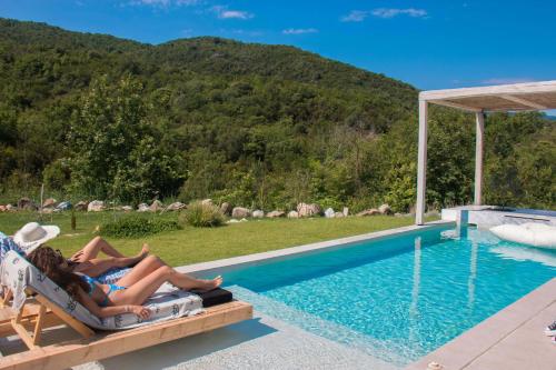 two people laying in chairs next to a swimming pool at Aristotelia Gi - Premium Luxury Villas with Private Pools in Olympiada