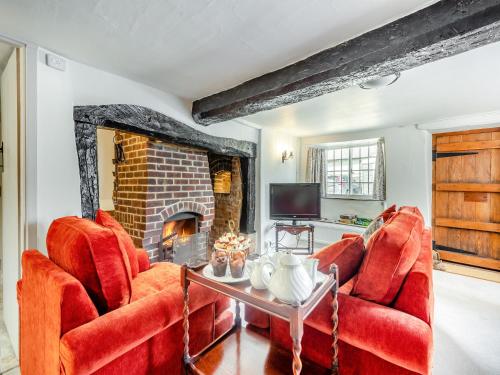 a living room with two red chairs and a fireplace at Hazel Cottage in Tolpuddle