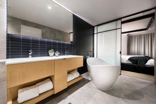 a bathroom with a tub and a sink and a bed at Tradewinds Hotel and Suites Fremantle in Fremantle