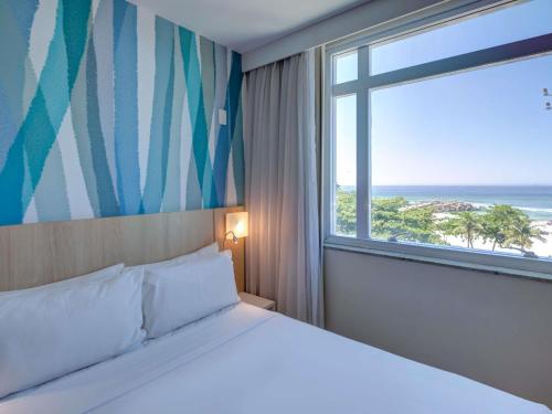 a bedroom with a bed and a large window at Mercure Rio de Janeiro Barra da Tijuca in Rio de Janeiro