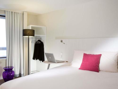 a bedroom with a bed with a pink pillow and a laptop at ibis Styles Lille Centre Gare Beffroi in Lille