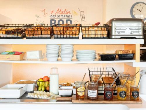 two shelves of a kitchen with plates and food at ibis budget Mâcon Nord in Mâcon