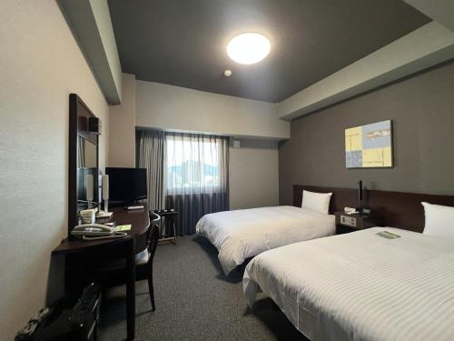 a hotel room with two beds and a desk and a television at Hotel Route-Inn Tokuyama Ekimae in Shunan