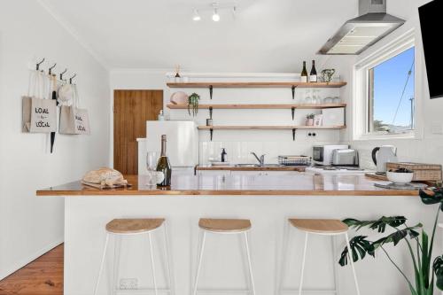 a white kitchen with a counter and stools at Beachfront Apartment at Apollo in Apollo Bay