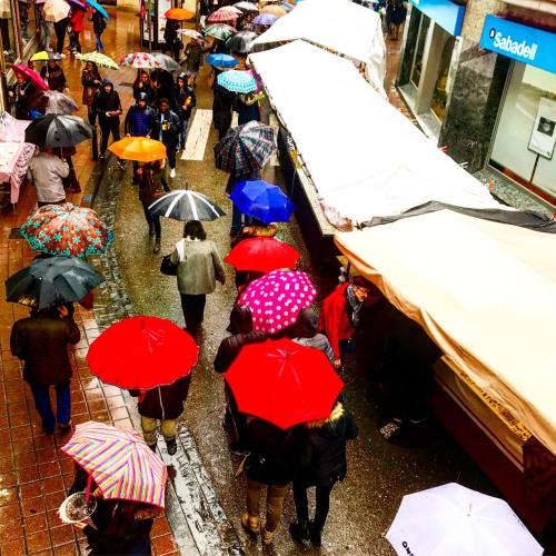 a group of people walking down a street holding umbrellas at Hostal Pirineos in Barbastro