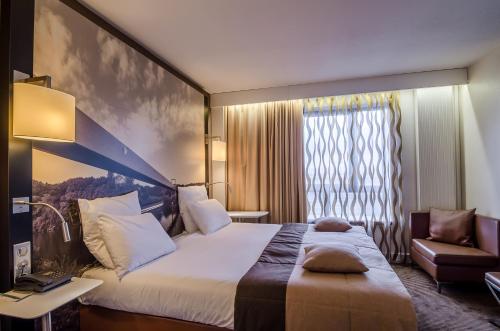 a hotel room with a large bed and a chair at Mercure Cergy Pontoise Centre in Cergy