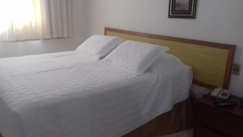 a bedroom with a bed with white sheets and a phone at Obeid Plaza Hotel in Bauru