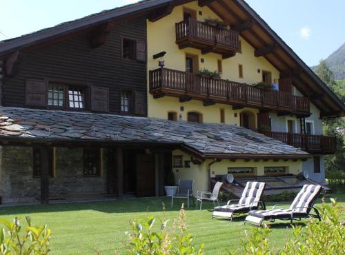 a house with a balcony and chairs in the yard at La Luge D'Antan Maison d'Hôtes & SPA in Brusson