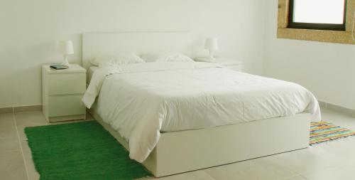 a white bedroom with a white bed with a green rug at Quinta de Gildinho in Gildinho