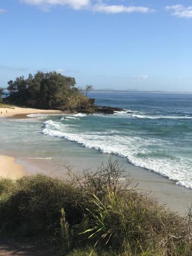 a beach with the ocean and trees in the distance at Oxley Cove Holiday Apartment in Port Macquarie