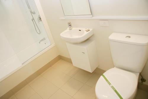 a white bathroom with a toilet and a sink at Oceans Resort Whitianga in Whitianga