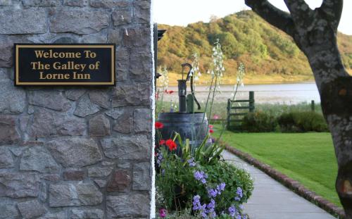 a sign on the side of a stone wall with flowers at The Galley Of Lorne Inn in Ardfern