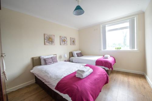 ペイズリーにあるPREMIER - Park View Apartmentのピンクの毛布が備わる客室内のベッド2台