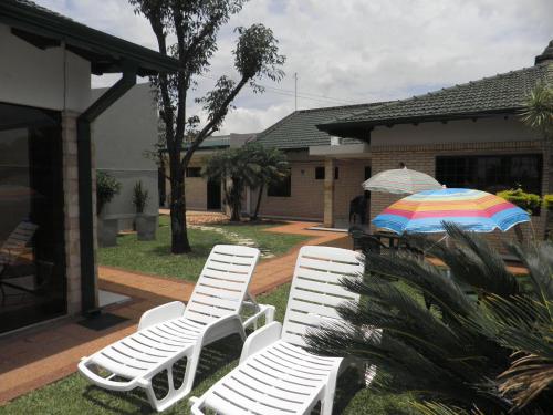 two white lawn chairs and an umbrella in a yard at Hotel Las Residentas in Luque