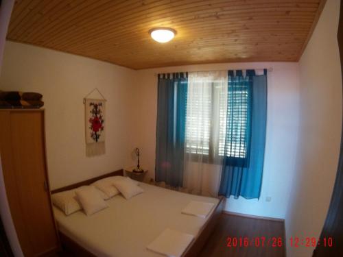a bedroom with a bed and a window with blue curtains at Apartman Luburić in Pinezici